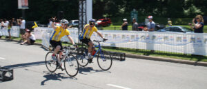 Brent and Ray riding bicycles through the finish line for the Ride to Conquer Cancer